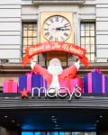 Santa figure with gifts and "Believe in The Wonder" banner above Macy's store entrance.