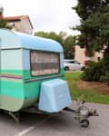 Vintage blue and green caravan parked on a street with trees and buildings in the background.