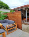 Modern tiny house with wooden exterior, sliding glass doors, and outdoor seating area with gray cushions.