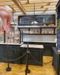 Hand arranging miniature pastries in a model bakery with black counters, white tiles, and hanging lights.