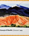 Postage stamp featuring a colorful landscape painting by Georgia O'Keeffe with mountains and red hills.