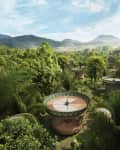 Circular treehouses with patterned roofs nestled in lush tropical forest, mountains in the background.