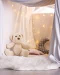 Cozy blanket fort with a teddy bear, string lights, and pillows on a fluffy rug.