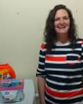 Woman in striped shirt standing beside laundry products on a washing machine.