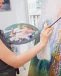 Artist painting a colorful abstract canvas with a palette in hand.