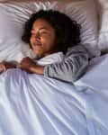 Woman sleeping peacefully in bed with white pillows and sheets.