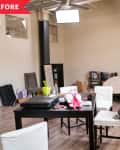 Cluttered living room with a black table, white chairs, TV, books, and scattered items on the floor.