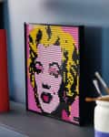 Pop art portrait made of small colored tiles on a shelf with art supplies and a pink flower.