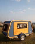 Wooden and blue teardrop trailer parked on grassy shore with ocean view.