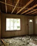 Unfinished room with exposed ceiling beams, debris on floor, large window, and closed door.