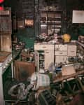 Cluttered kitchen with damaged cabinets, debris, and scattered household items.