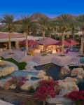 Luxurious outdoor patio with palm trees, pink canopies, pool, and vibrant bougainvillea, set against mountain backdrop.
