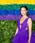 Woman in a purple dress standing in front of a colorful floral wall with yellow, green, blue, and purple roses.