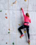 Person in pink shirt climbing an indoor rock wall with colorful holds.