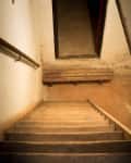 Dimly lit staircase leading to a basement with a wooden bench at the bottom.