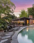 Mid-century modern house with a pool, surrounded by lush greenery and bamboo, under a vibrant sunset sky.