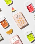 Colorful Touchland hand sanitizers and packaging with fruit slices and leaves on a light surface.