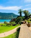 Wooden deck with potted plants overlooking a lush garden and beach, with mountains in the background.