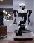 Robot with black and white design holding a green sponge in a modern office setting.