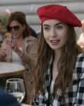 Woman in red beret and checkered jacket sitting at an outdoor café table.