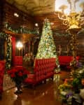 Lavishly decorated library with a Christmas tree, red chairs, a roaring fireplace, and ornate chandeliers.