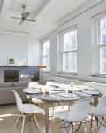 Open-plan living room with gray sofa, round dining table, white chairs, bookshelves, and large windows.