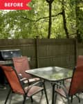 Patio with glass table, four red chairs, grill, and wooden fence surrounded by trees.