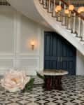 Grand staircase with wooden railing, marble table, large flower decor, and black double doors in an elegant foyer.