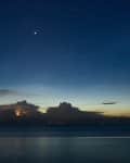 Night sky over calm ocean with distant clouds and visible stars.