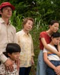 Family of five standing together in a grassy field, looking contemplative.