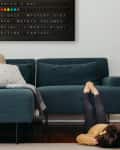 Child lying on floor with feet up on a teal sofa, under a wall-mounted letter board.
