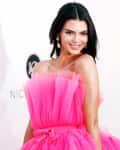 Woman in a vibrant pink strapless gown with tulle details, smiling at an event.