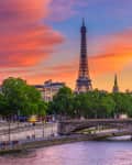 Eiffel Tower at sunset with vibrant sky, Seine River, and bridge in Paris.