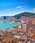 Coastal view of Split, Croatia, featuring turquoise waters, marinas, and terracotta-roofed buildings against a hillside.
