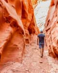 Person walking through a narrow red rock canyon with textured walls.