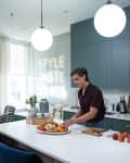 Man preparing food in a modern kitchen with teal cabinets, white countertops, and a neon sign reading "STYLE TASTE CLASS."