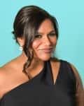 Woman in a black one-shoulder dress with earrings, smiling against a turquoise background.