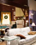 Cozy living room with floral sofa, wooden coffee table, vintage kitchen, and colorful decor accents.