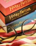 Harry Potter books stacked on a Gryffindor scarf with round glasses.
