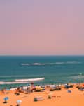 Crowded beach with colorful umbrellas, people sunbathing, and a parasailer over the ocean.
