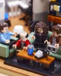 Four LEGO figures sitting on a green sofa in a living room, with a coffee table and bookshelf in the background.