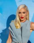 Blonde woman in a light blue dress with red lipstick, standing against a blue background.