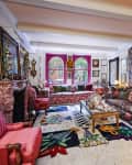 Eclectic living room with floral sofas, vibrant rugs, ornate fireplace, and art-filled walls.