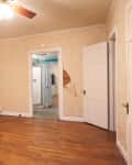 Empty room with hardwood floors, beige walls, ceiling fan, open closet, and visible damage near doorways.