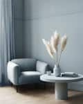 Cozy living room with a gray armchair, round table, pampas grass in a vase, and a cup on a wooden floor.