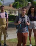 Three teenagers with backpacks standing on a suburban street, facing an unseen person.