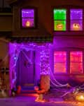 House decorated for Halloween with purple lights, cobwebs, and glowing pumpkins in windows and yard.