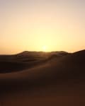 Sunset over sand dunes with footprints leading into the distance.