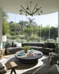 Curved gray sofa in a living room with large windows, round coffee table, modern chandelier, and vibrant artwork.