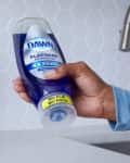 Hand holding Dawn Platinum dish soap bottle with hexagonal tile backsplash.